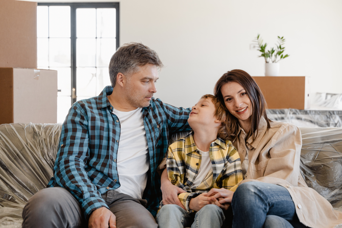 Three people sit on a couch, smiling and hugging in a bright living room