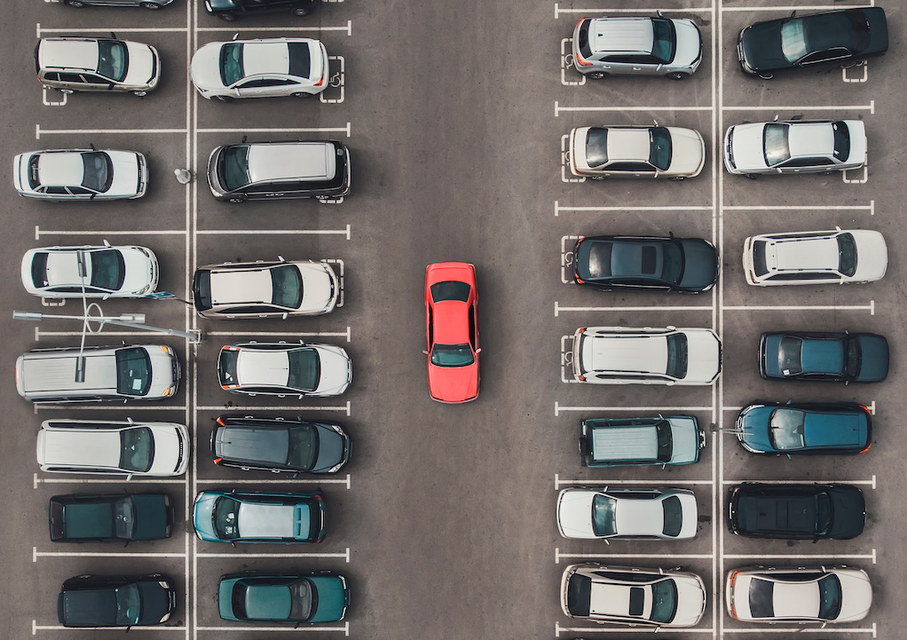 An aerial view of a parking lot with a red car in the middle.