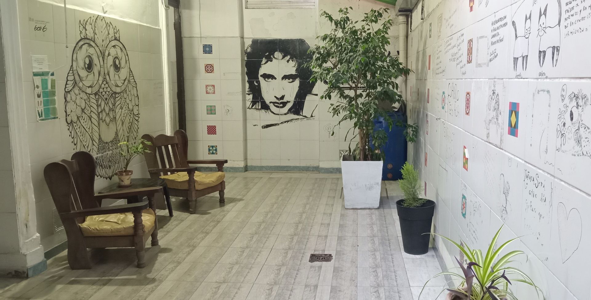 Salón moderno con sillas, plantas en macetas y mural en un luminoso pasillo interior.