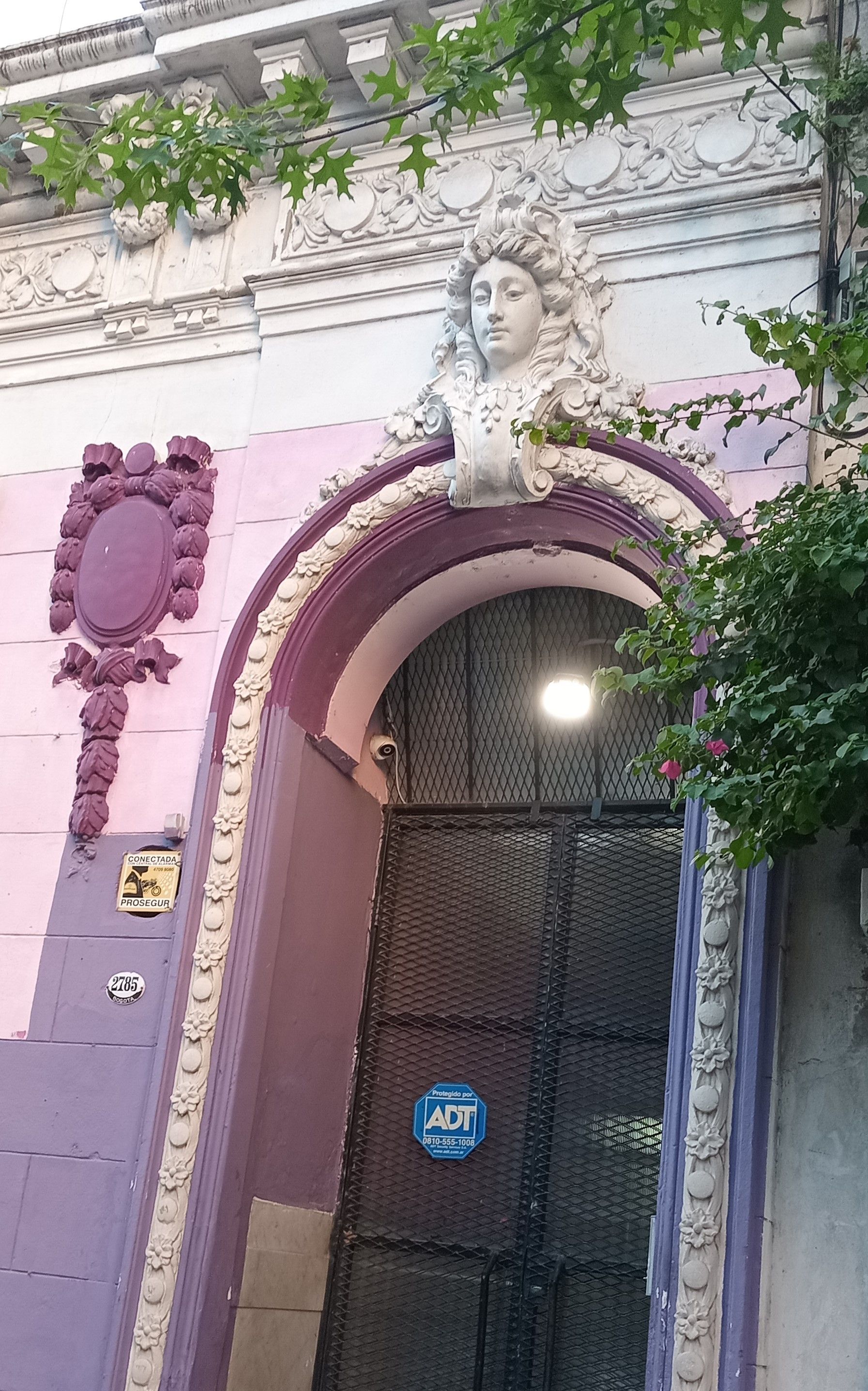 Entrada del edificio color lavanda con una puerta arqueada ornamentada y una escultura decorativa de un rostro encima.