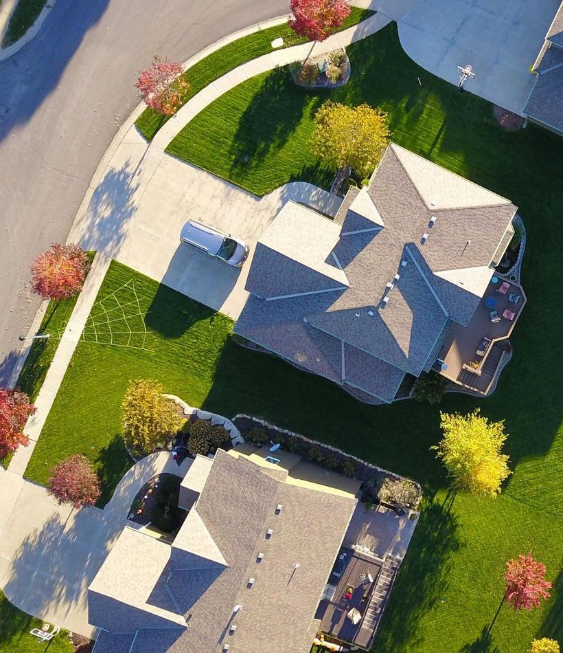 Aerial view of houses with green lawns and colorful autumn trees.