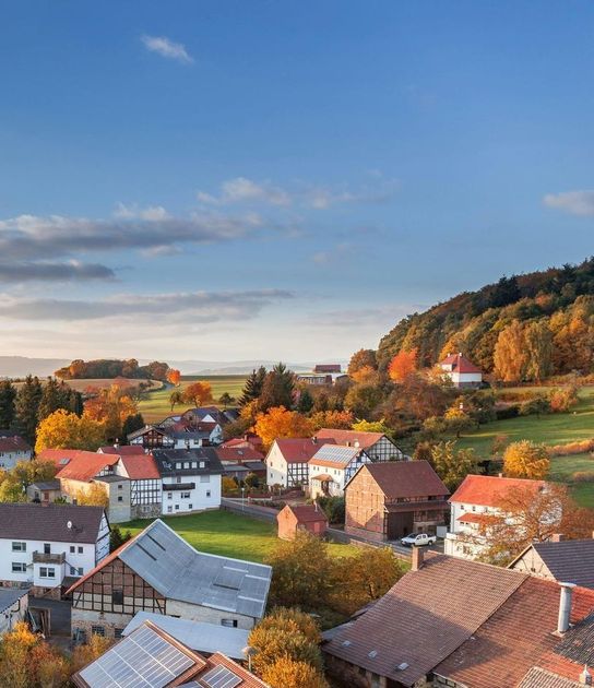 Village with colorful autumn trees and houses under a blue sky.