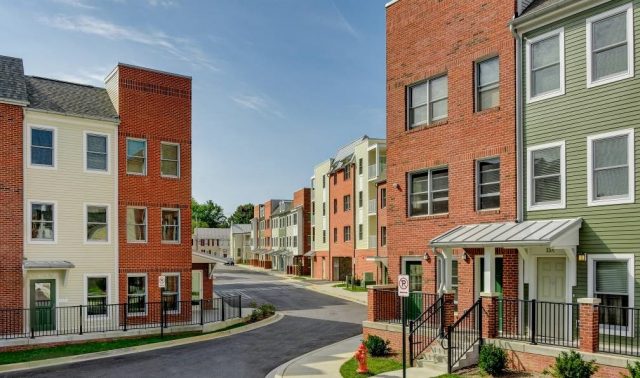 Row of townhomes with brick and green siding on a curved street under a blue sky.