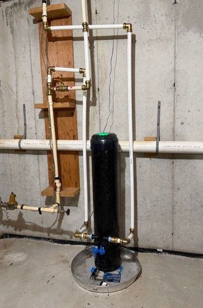 Basement utility setup with black water softener tank, copper pipes, and white plumbing lines.