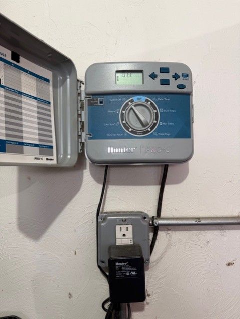 Wall-mounted white controller with LCD screen and dial, connected to a plug-in power adapter and open panel.