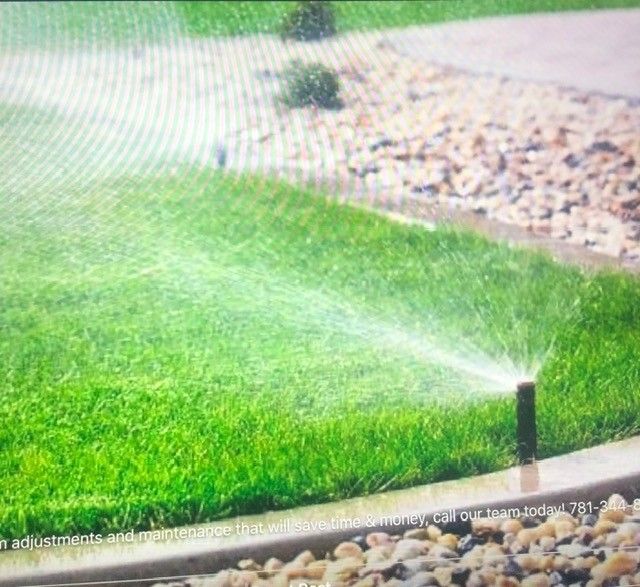 Sprinkler watering a green lawn beside a rock border and gravel path.