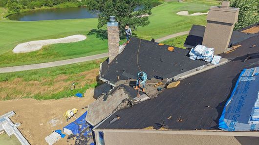 Roofers installing black shingles on a suburban house roof with ladders nearby