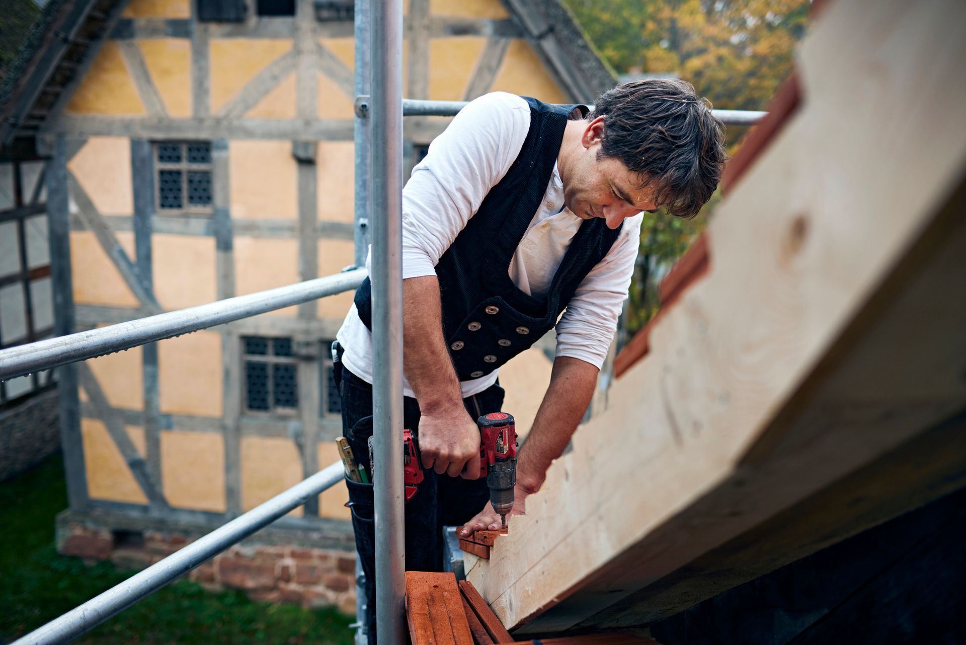 A roofer is using a drill on the roof of a house. A roofer is using a drill on the roof of a house.