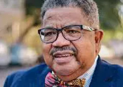 A man wearing glasses and a bow tie is smiling.