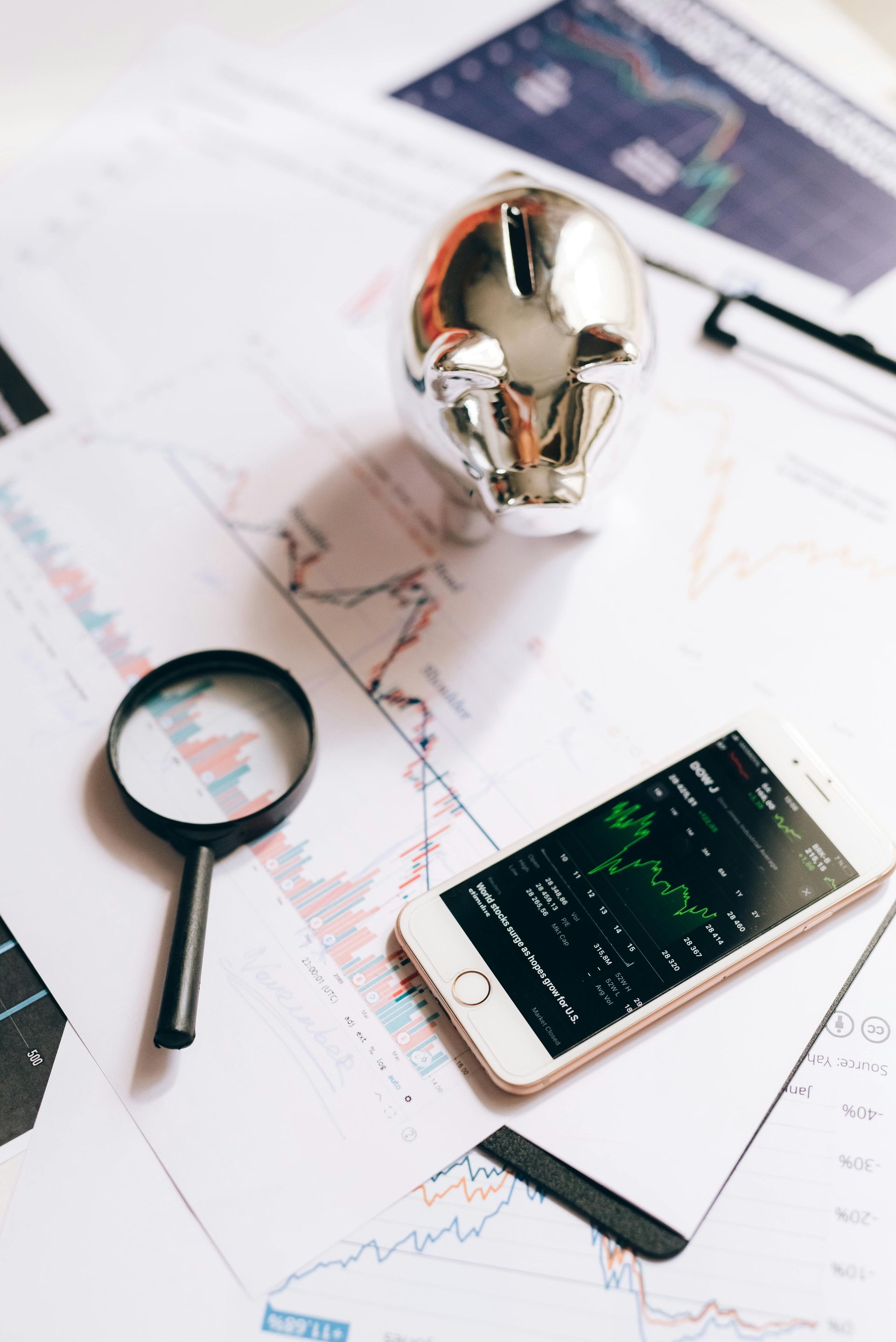A magnifying glass is on a table next to a cell phone and a piggy bank.