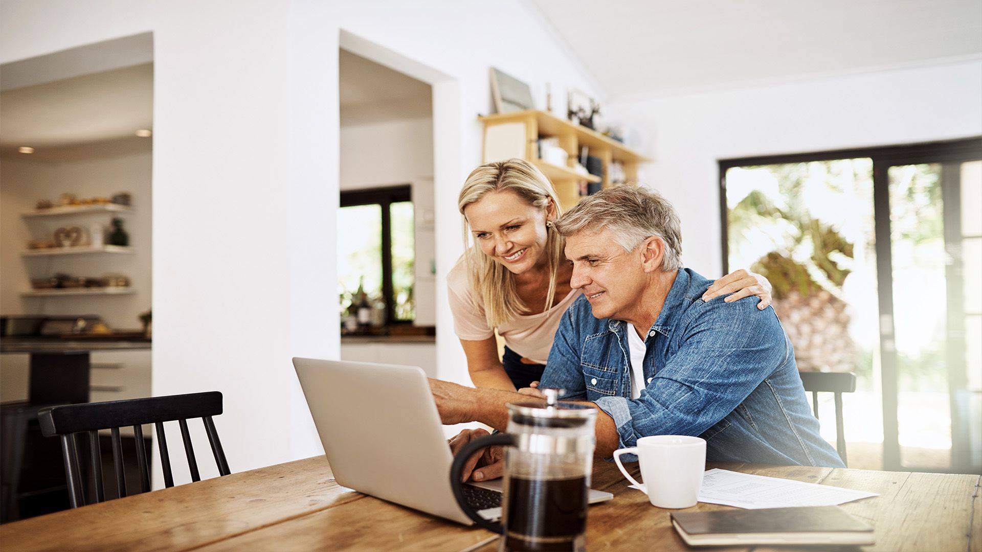 A man and a woman are sitting at a table looking at a laptop computer.