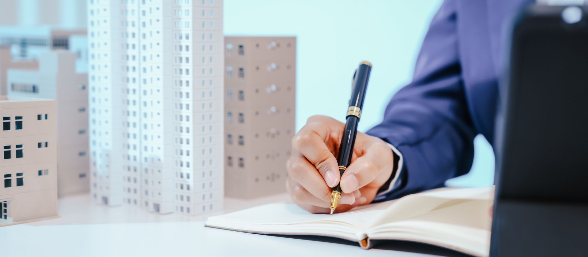 Une personne en costume bleu écrit dans un carnet à côté d'une maquette d'immeubles de bureaux.