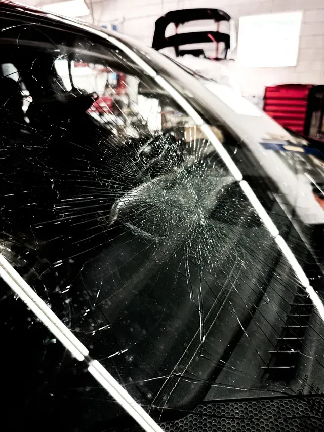 Cracked car windshield with spiderweb-like fractures radiating from an impact point.