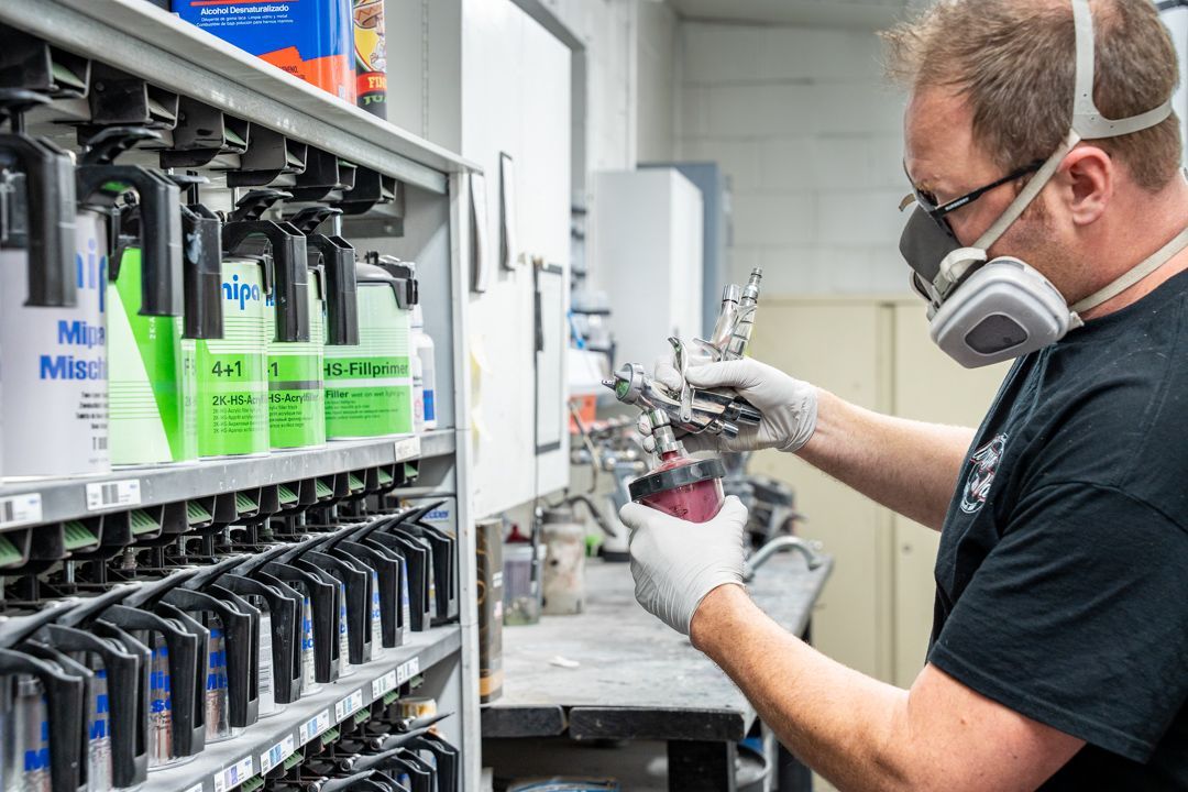 Man in respirator and gloves prepares to paint in a workshop, surrounded by paint bottles.