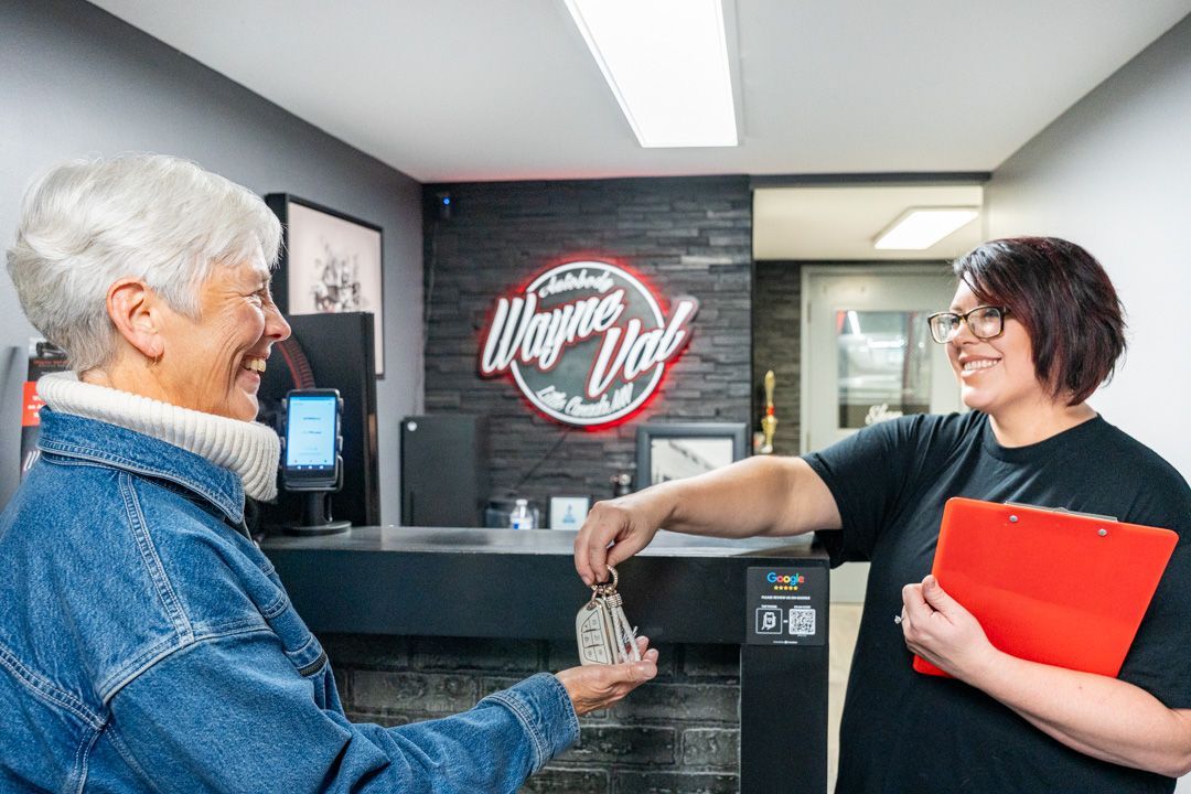 Woman handing keys to a person behind a counter at a business with a sign 