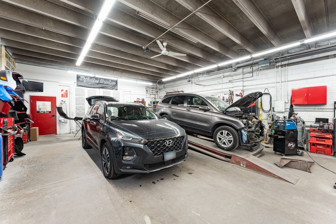 A car repair shop. Two cars, one gray, one black, in for service. Tools and equipment visible.