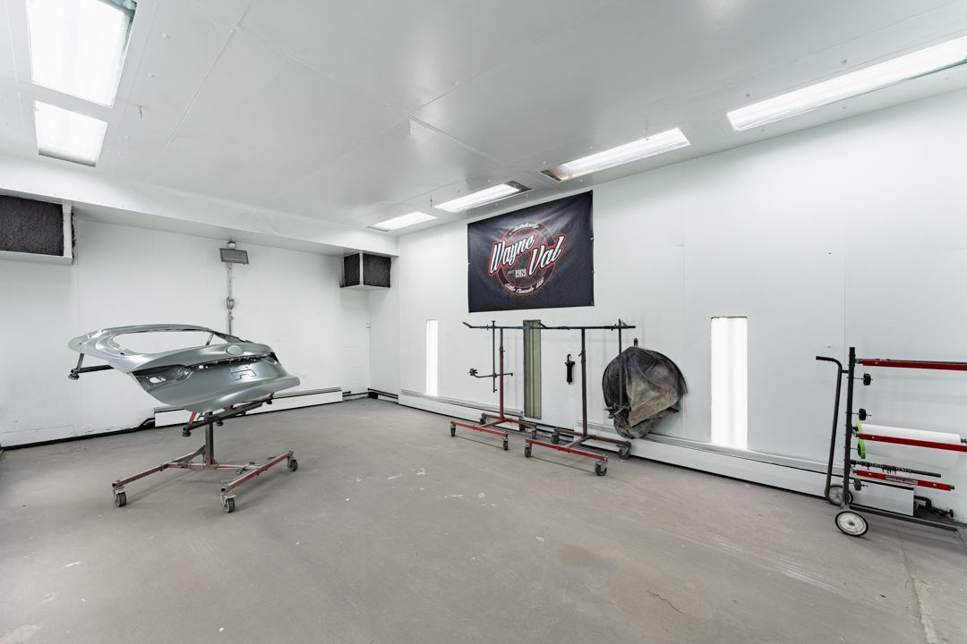 A car body repair shop with a car panel on a stand, tools, and a large poster on the wall.
