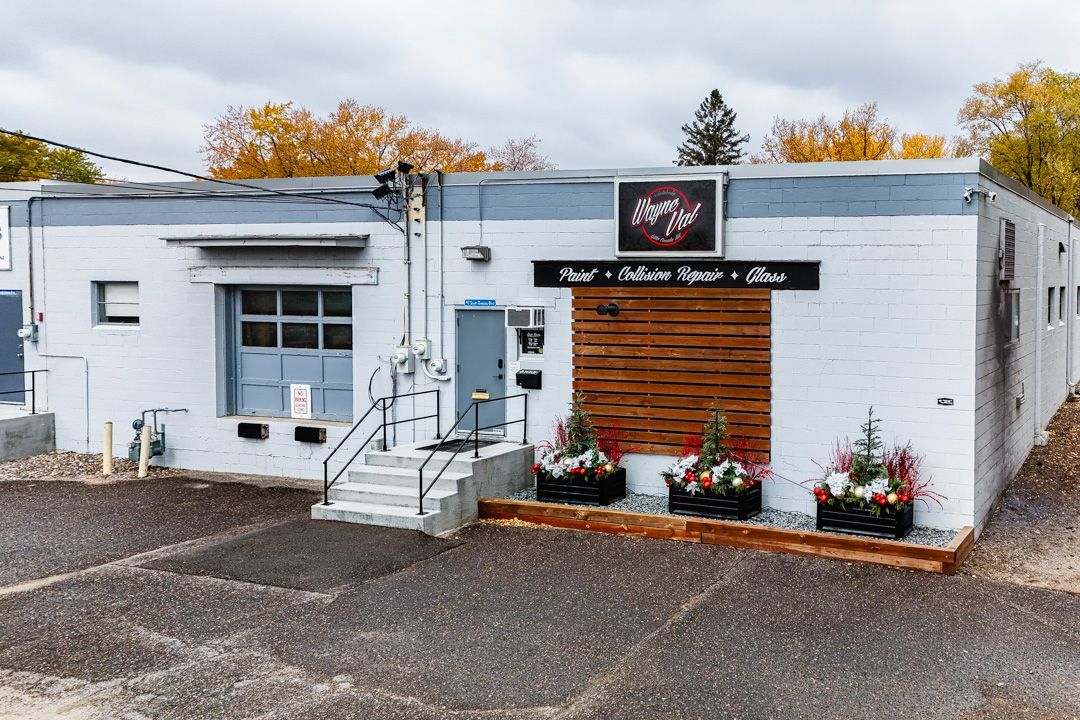 Exterior of a white commercial building with a wooden accent and flower planters. Sign says