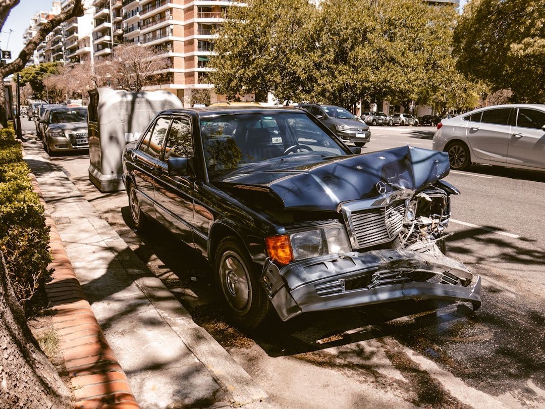 A dark blue car with severe front-end damage parked along a city street.