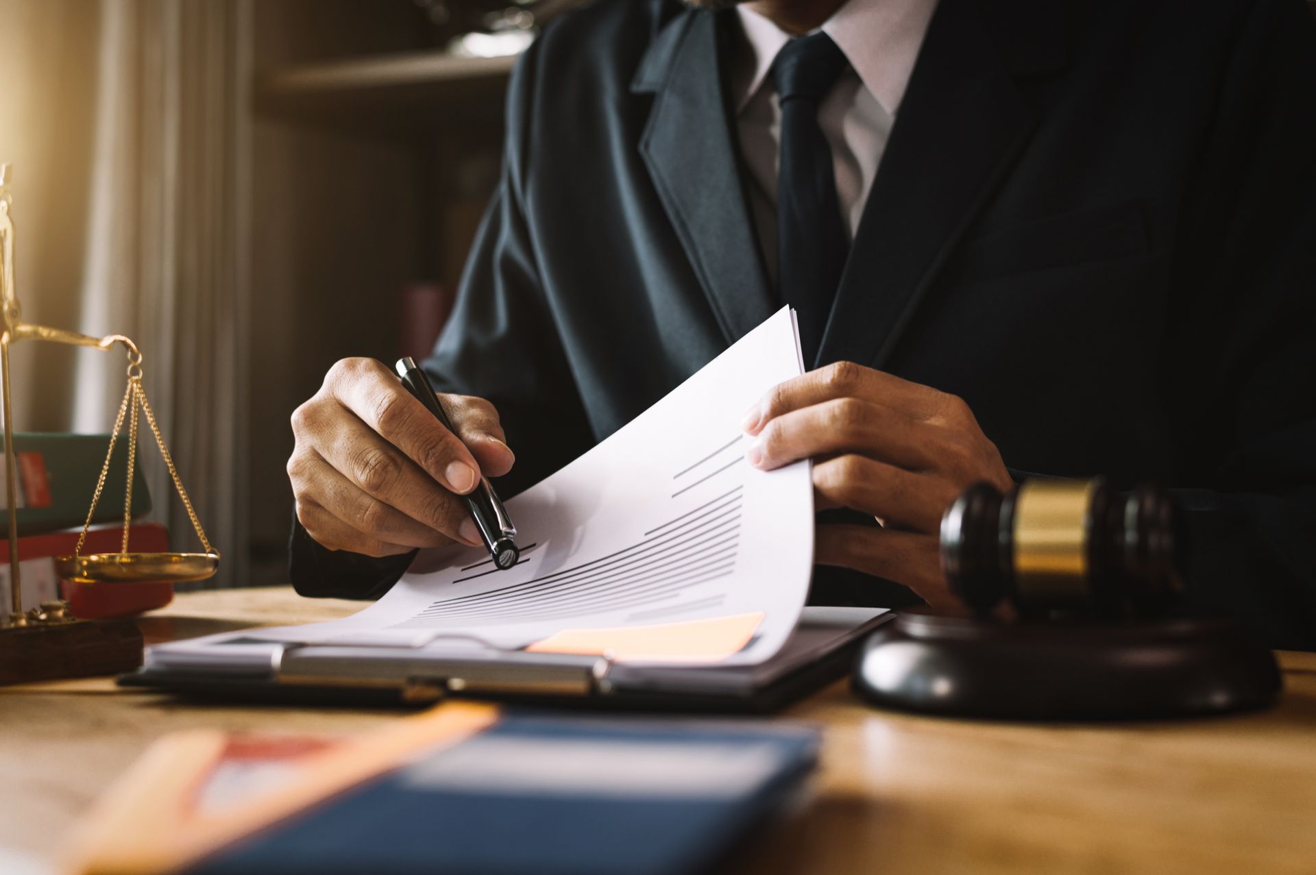 Businessperson signing a document at a desk with a gavel and scales of justice nearby