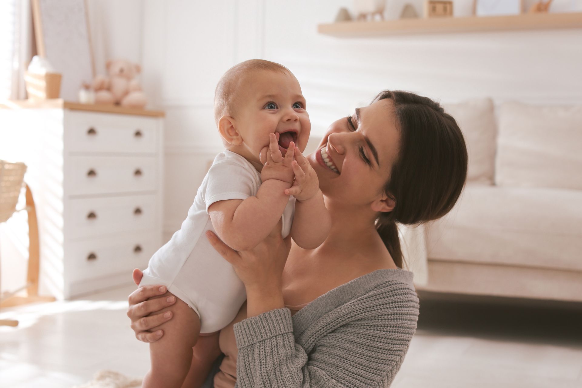 Woman holding smiling baby in a softly lit bedroom