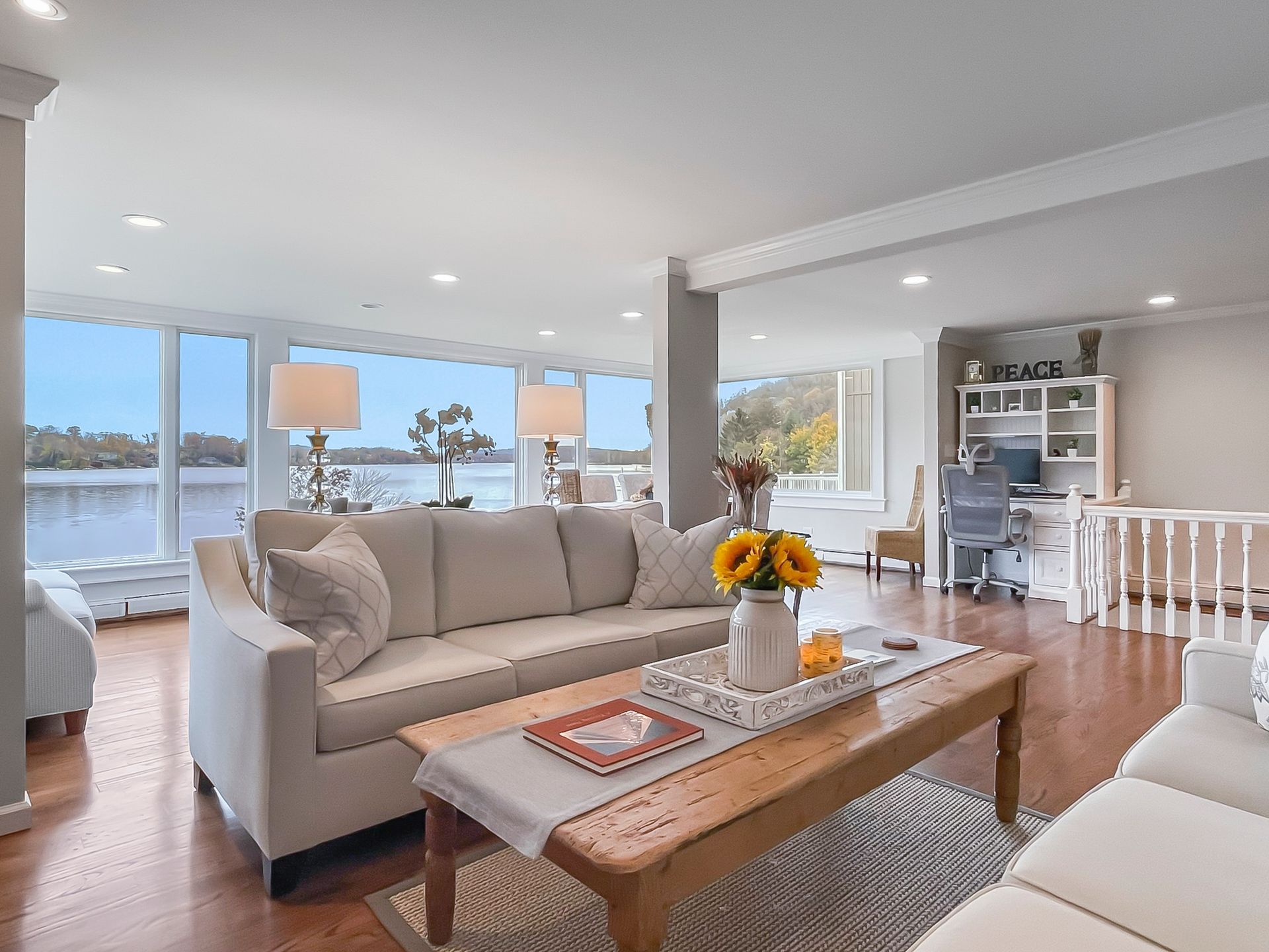 Bright living room with beige sofas, wooden coffee table, and large windows overlooking the water