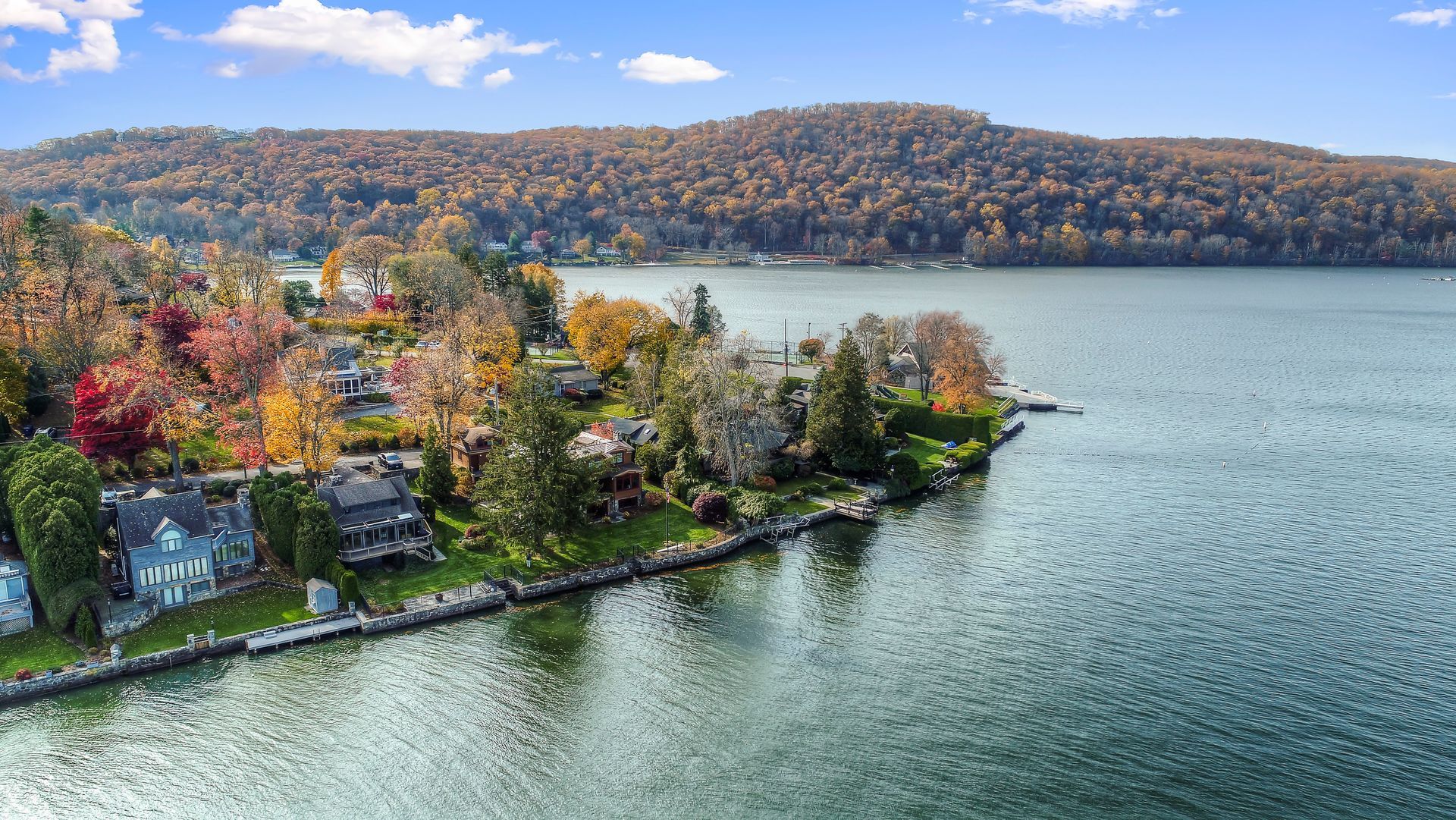 An aerial view of a lakeside neighborhood with autumn-colored trees along the shoreline and a large lake in the foreground.
