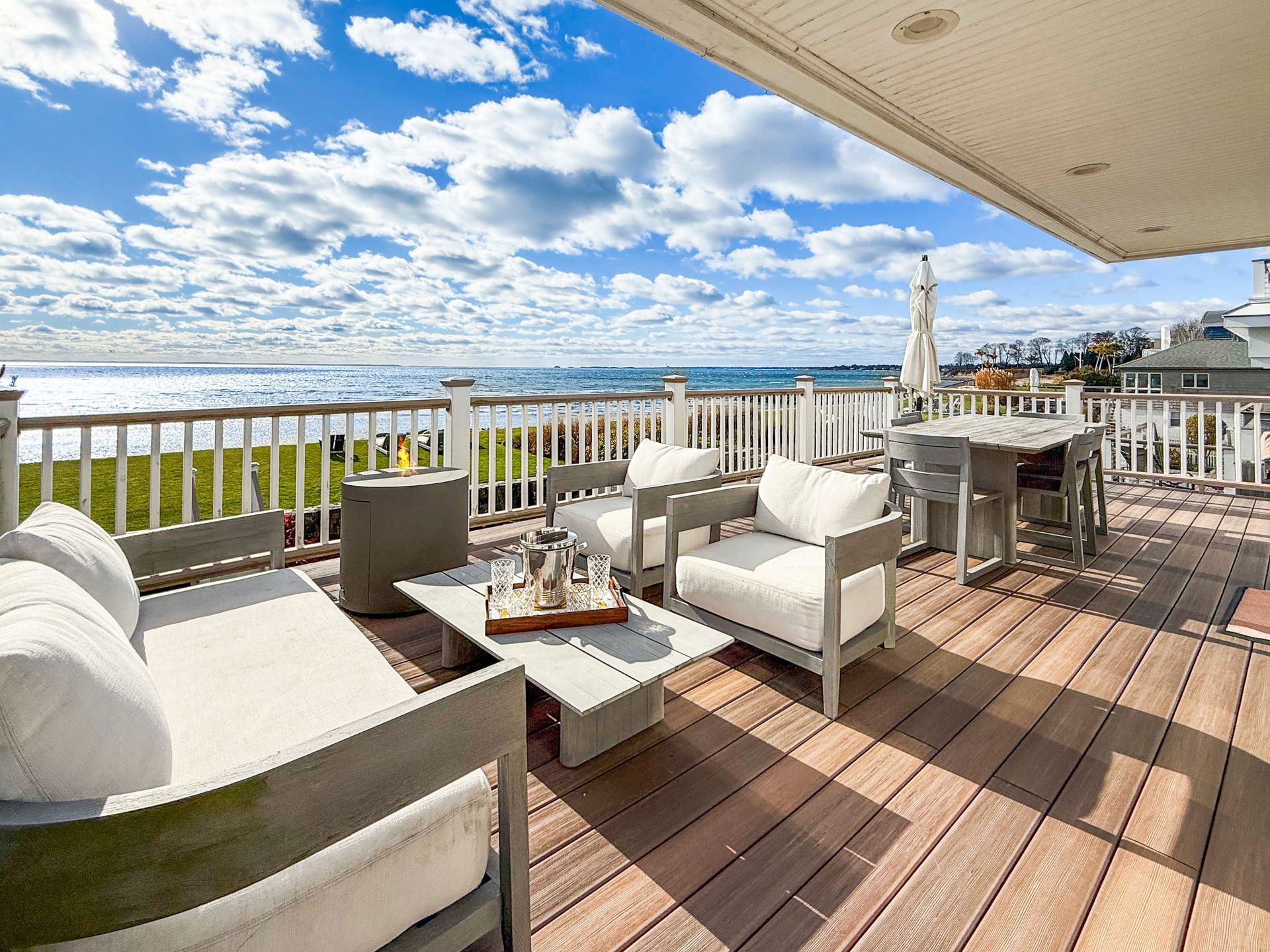 A patio with modern white seating overlooking the ocean under a bright, cloudy sky.