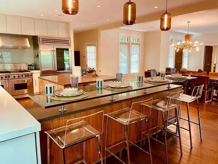 Modern kitchen featuring a breakfast bar with clear stools, warm wood cabinetry, and pendant lighting.