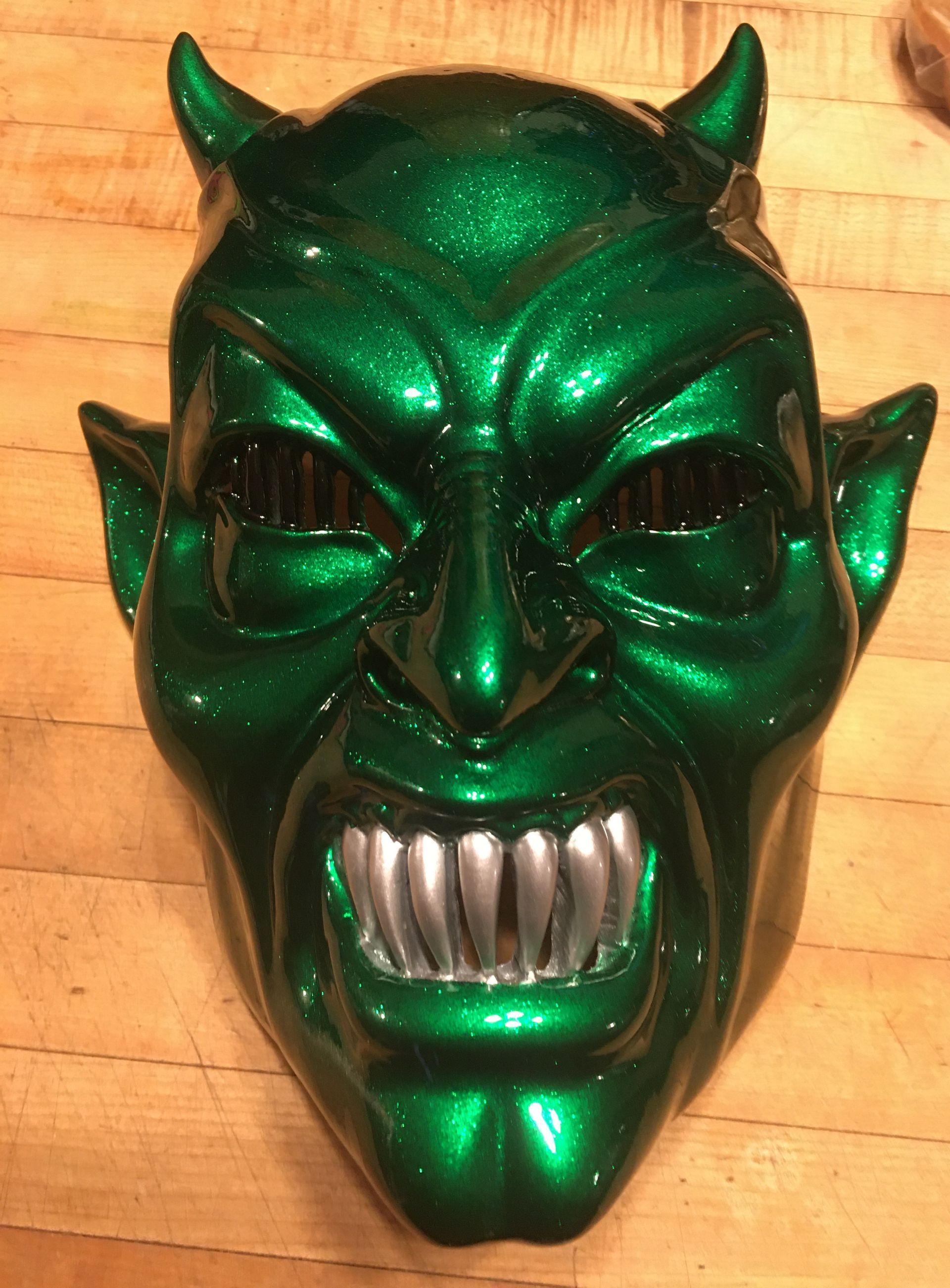 A green devil mask is sitting on a wooden table.