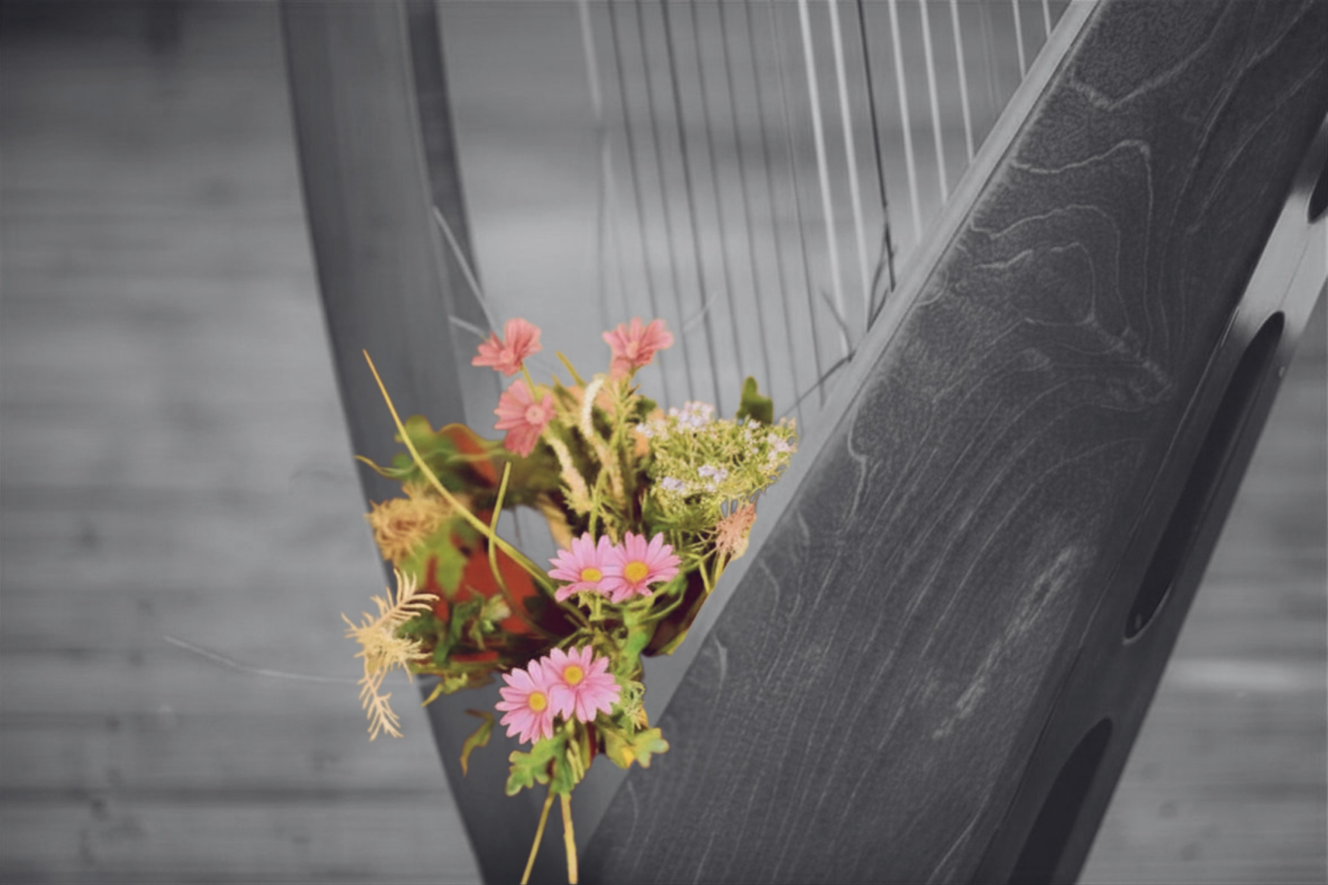 A dark wooden harp adorned with a small bouquet of pink and yellow flowers against a blurred grey background.