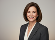 Professional woman in a dark blazer and white blouse, smiling against a neutral background