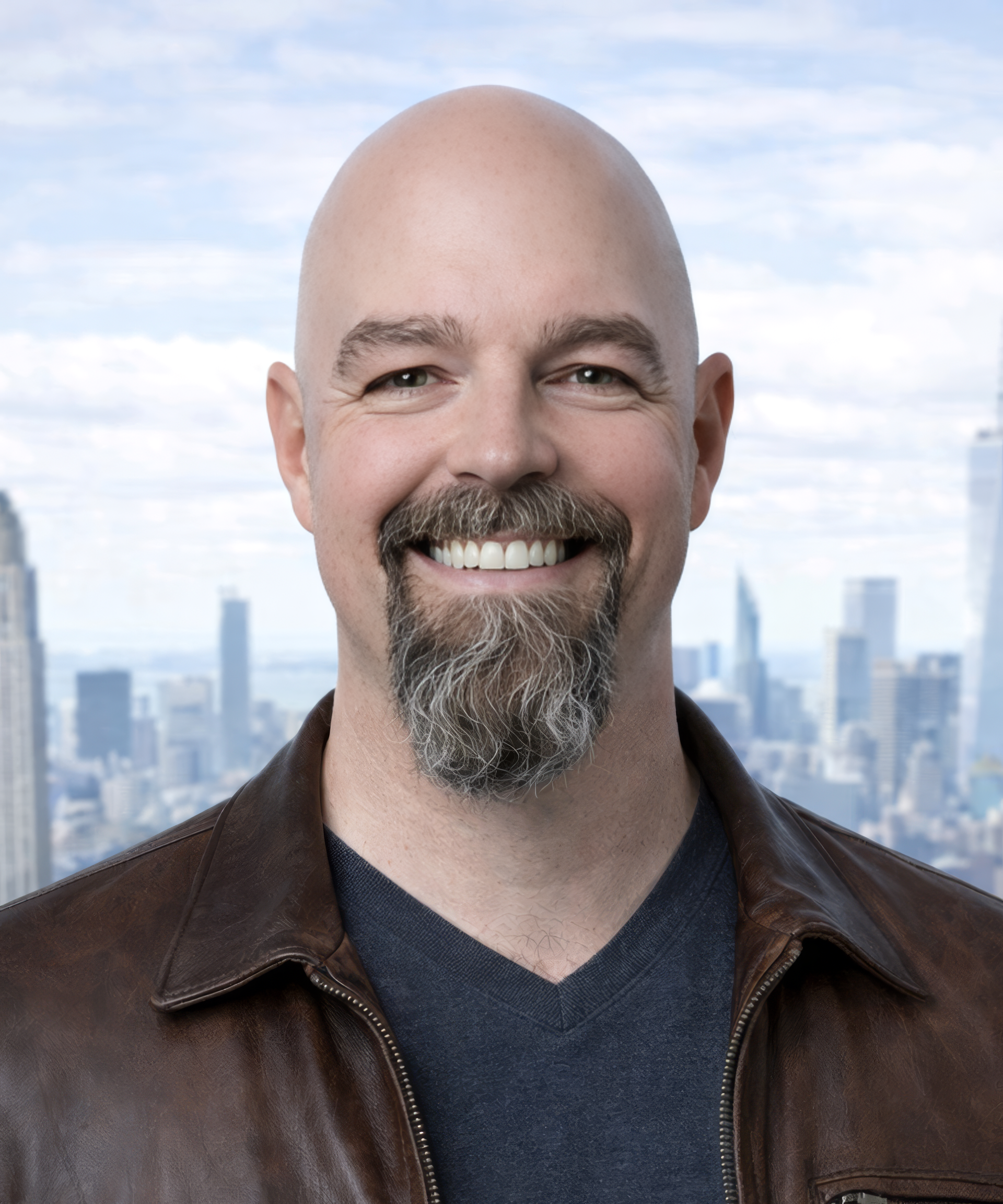 Smiling bald man with a goatee in a brown jacket, standing before a city skyline.