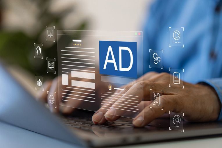 Person typing on a laptop with a blue “AD” overlay and digital icons on screen