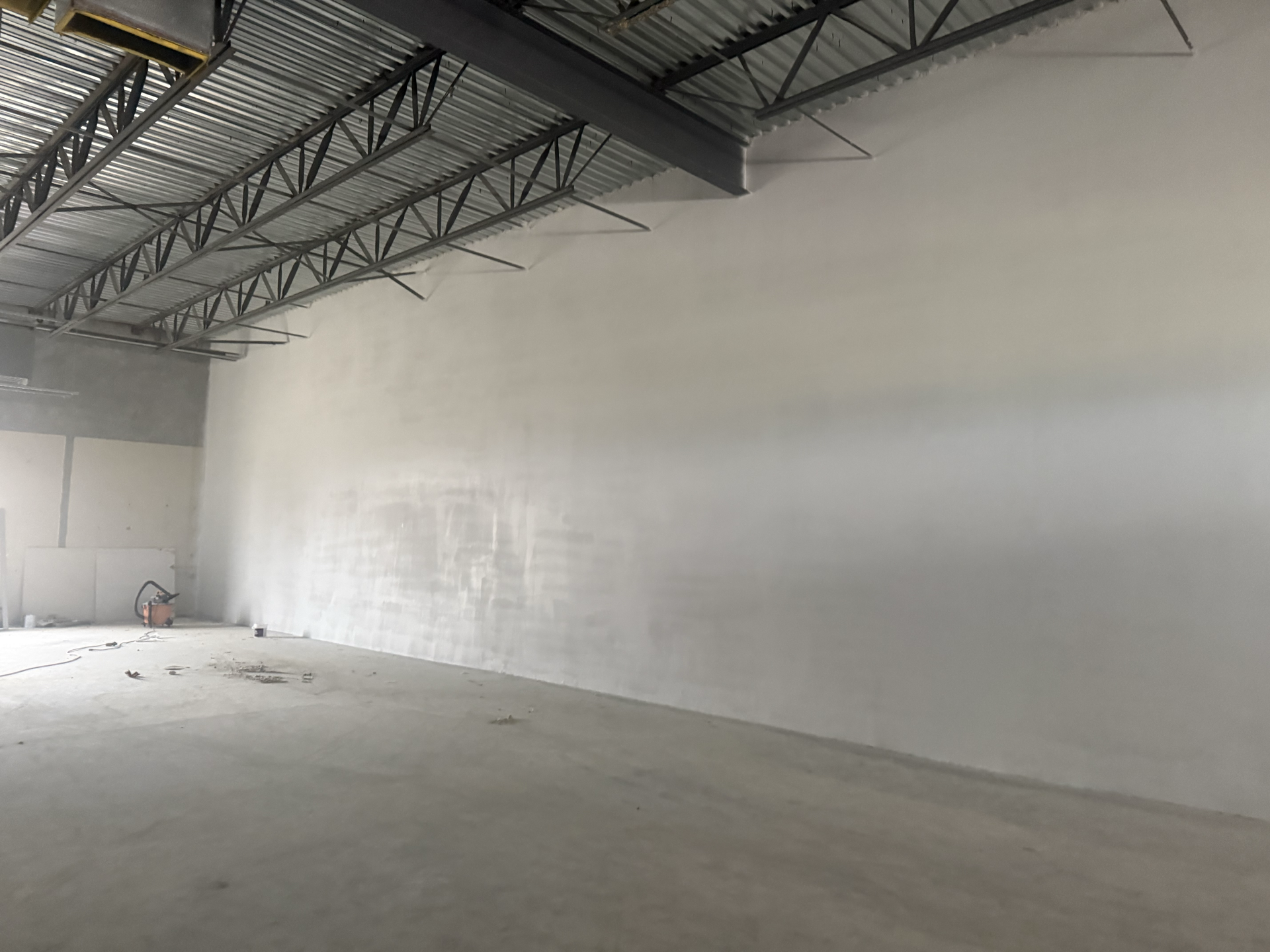 Empty, light-grey interior of a building under construction.  Concrete floor and smooth, white walls with metal ceiling.