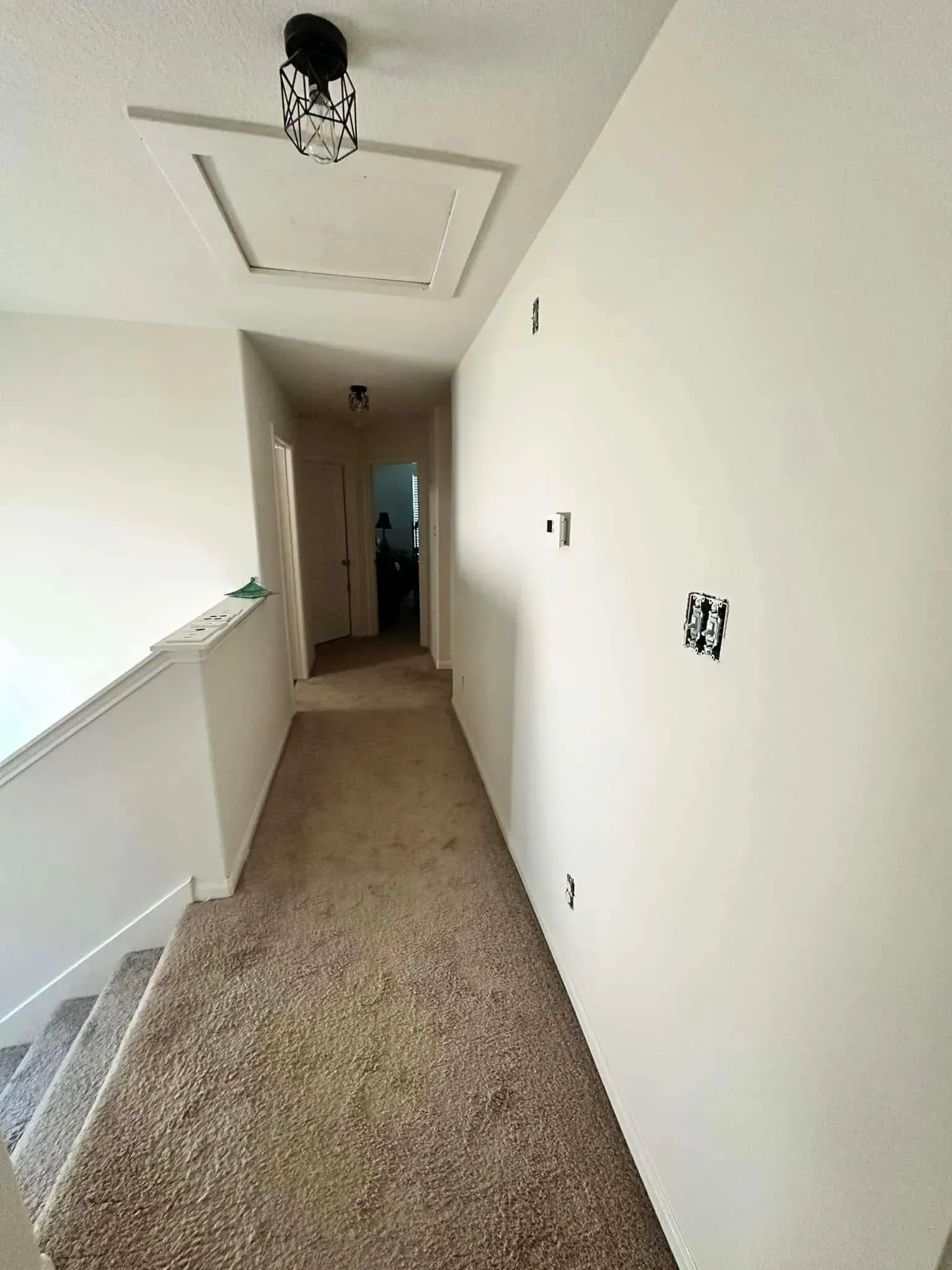 Hallway with carpet, white walls, light fixtures, and a staircase.