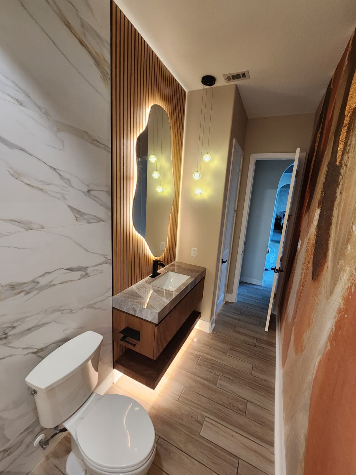 Modern bathroom with wood accent wall, lighted mirror, floating vanity, and toilet.