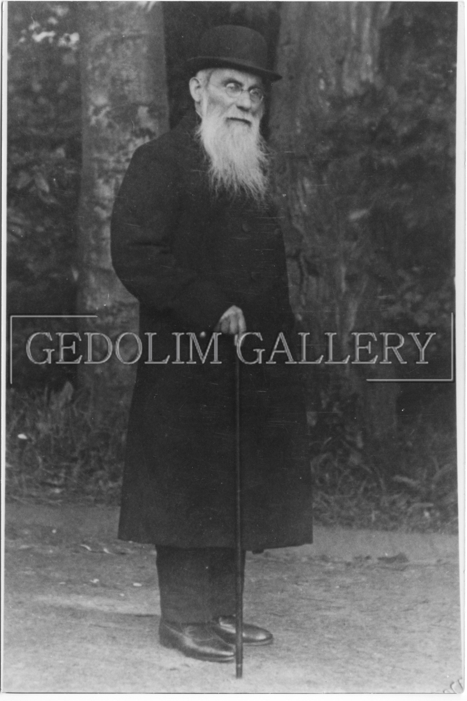 A black and white photo of a man with a beard holding a cane