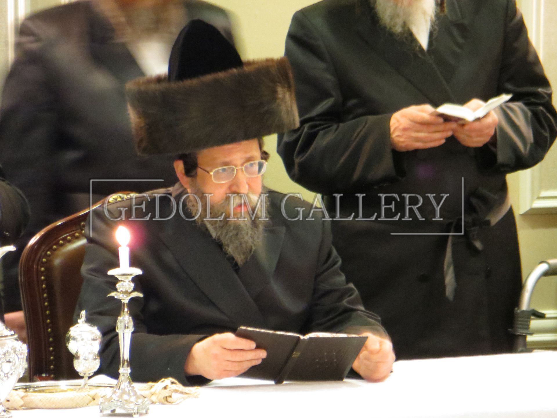 A man in a fur hat sits at a table with a lit candle in front of the word gallery