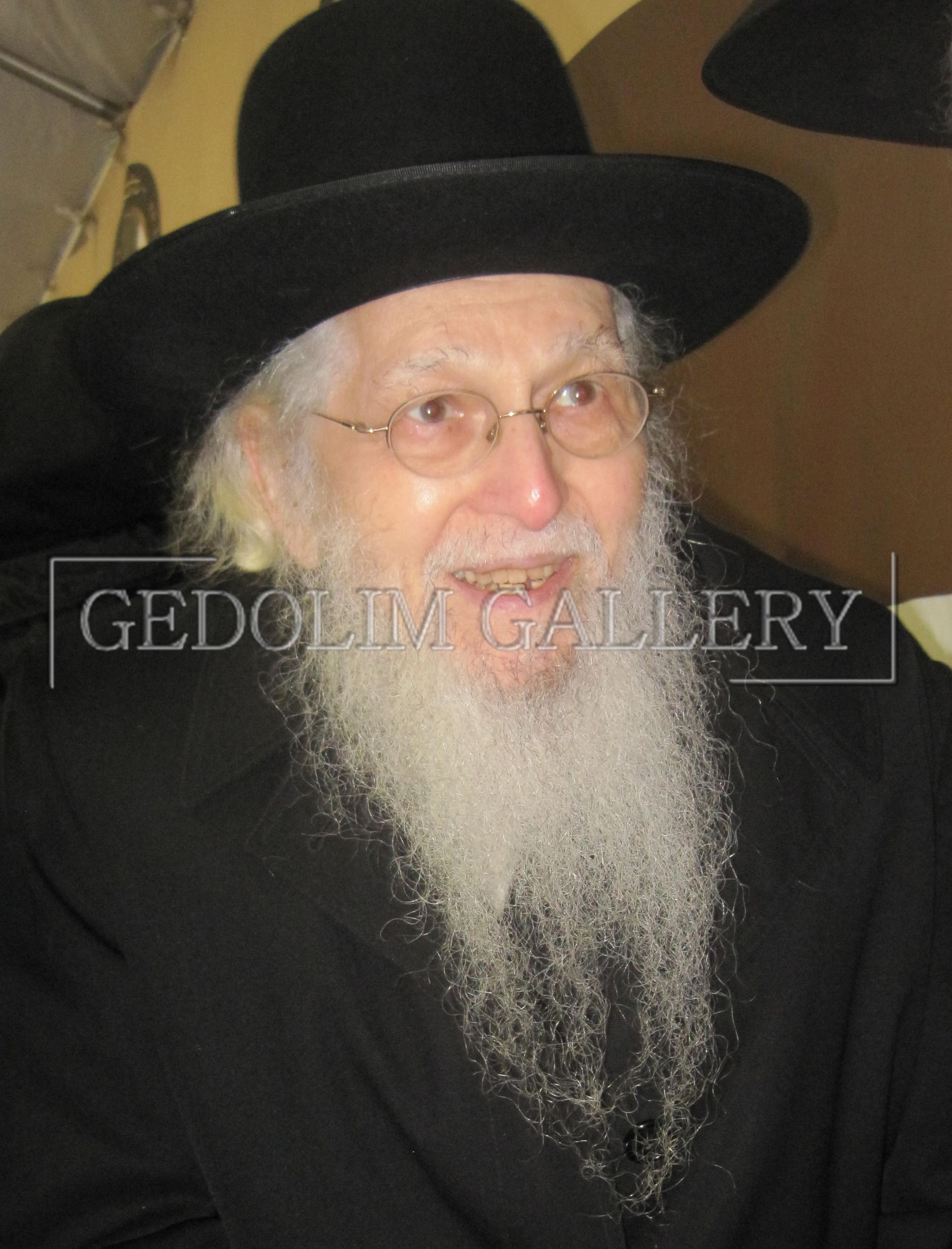 A man with a beard and glasses is wearing a black hat with the word gedolin gallery on the bottom