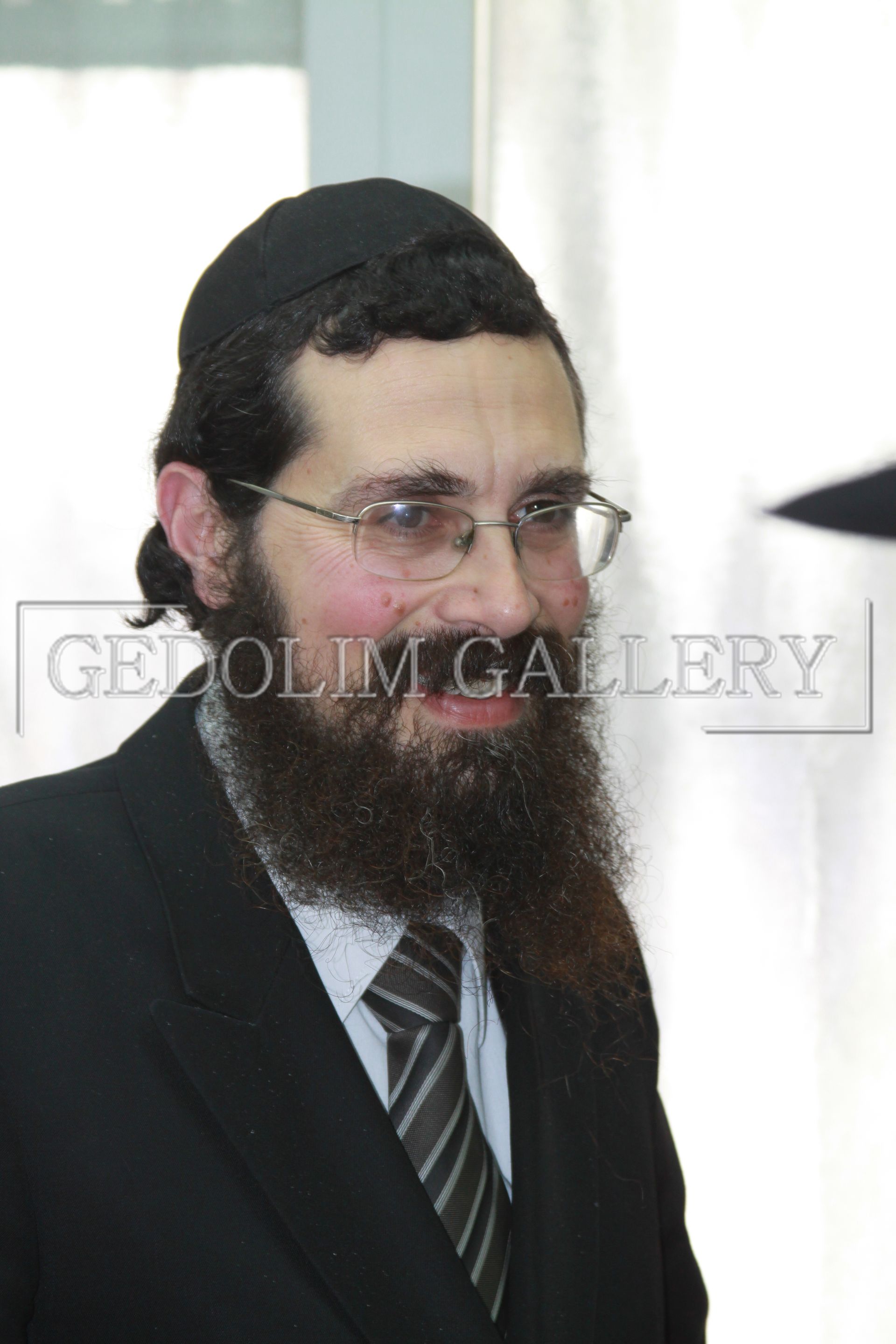 A man with a beard is wearing glasses and a black hat