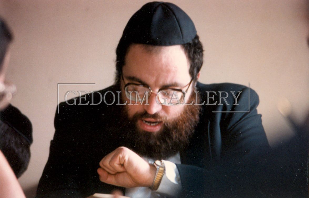 A man with a beard and glasses is wearing a black hat