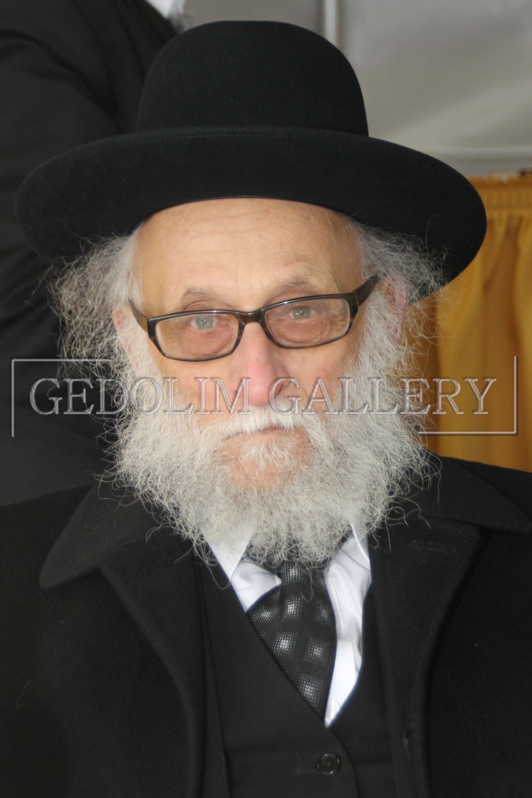 A man with a beard and glasses is wearing a black hat