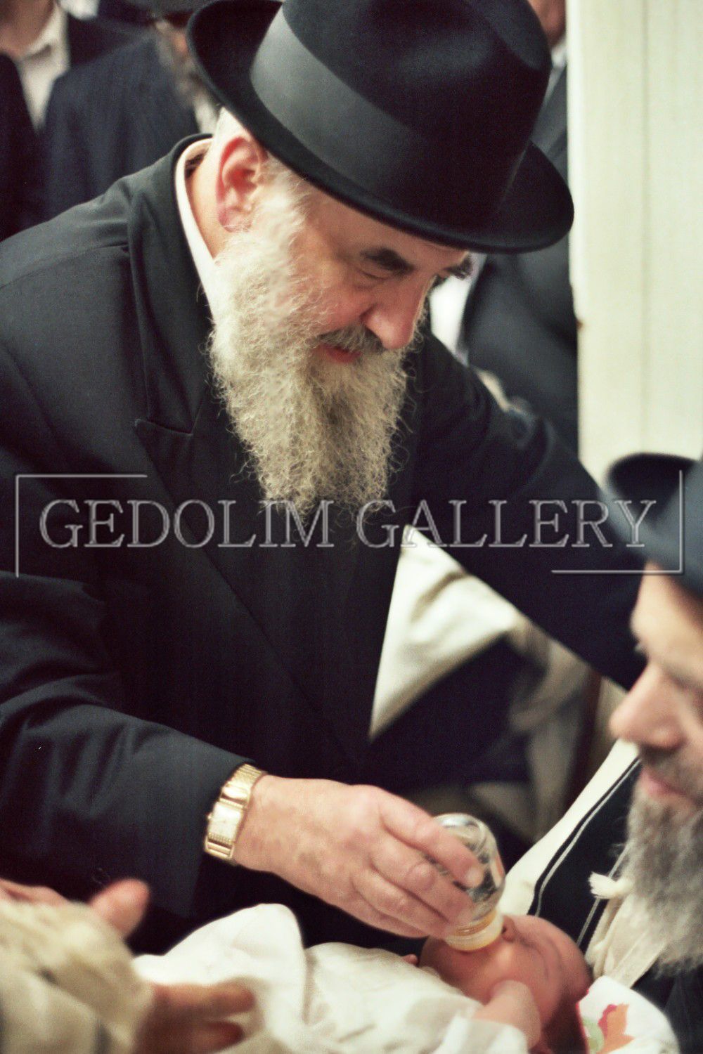 A man with a beard is feeding a baby from a bottle with the word gedolin gallery on the bottom