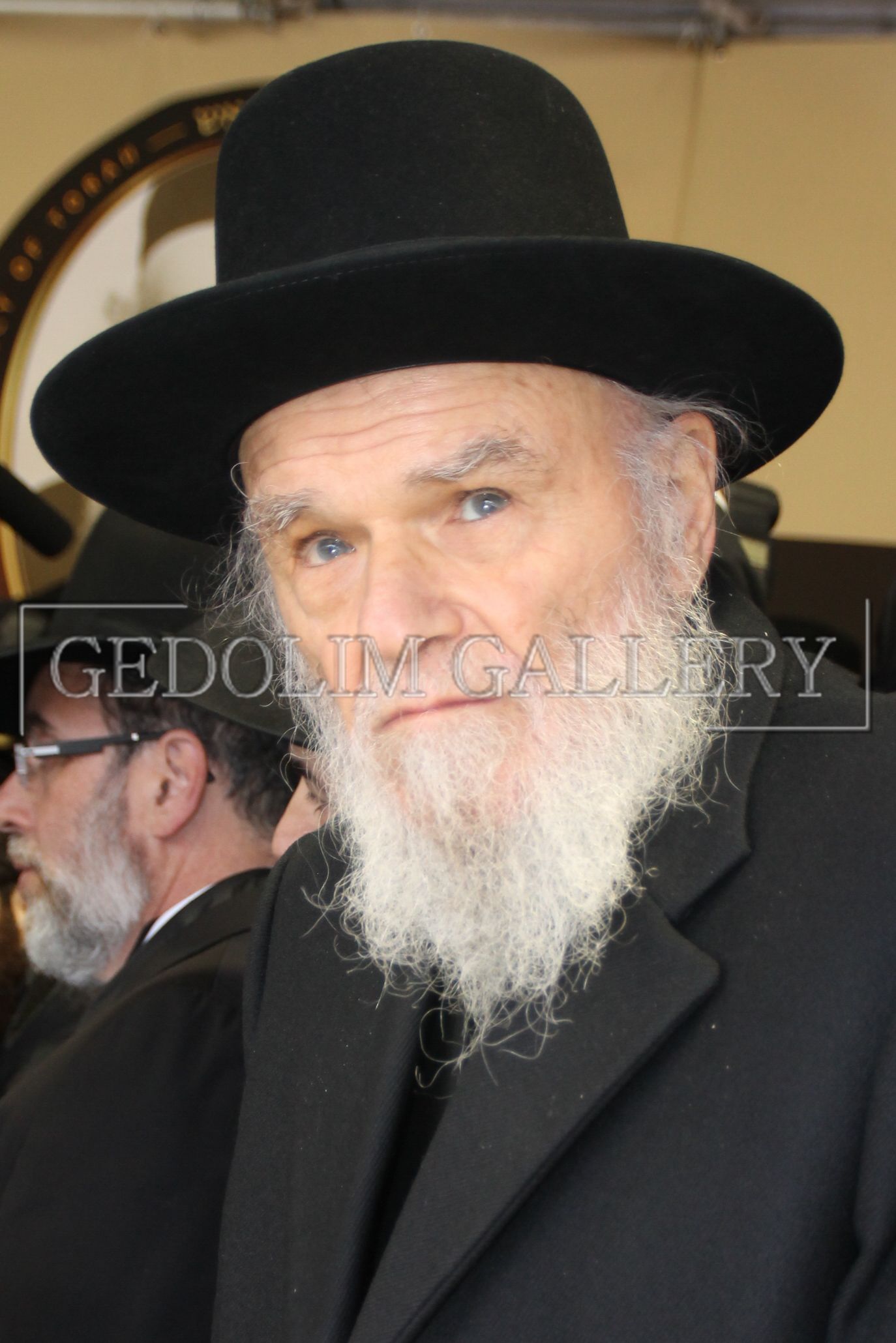 A man with a beard wears a black hat and a black jacket