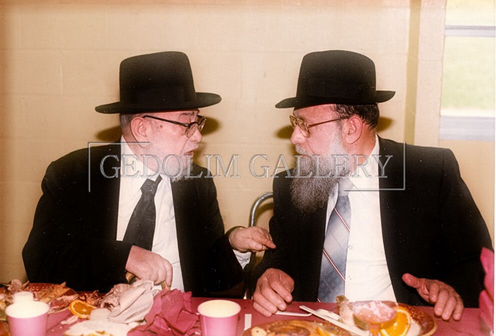 Two men in suits and hats are sitting at a table talking