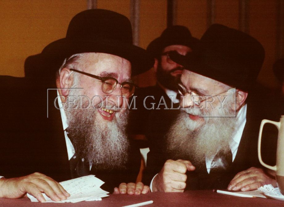 Two bearded men are sitting at a table and one is pointing at the other