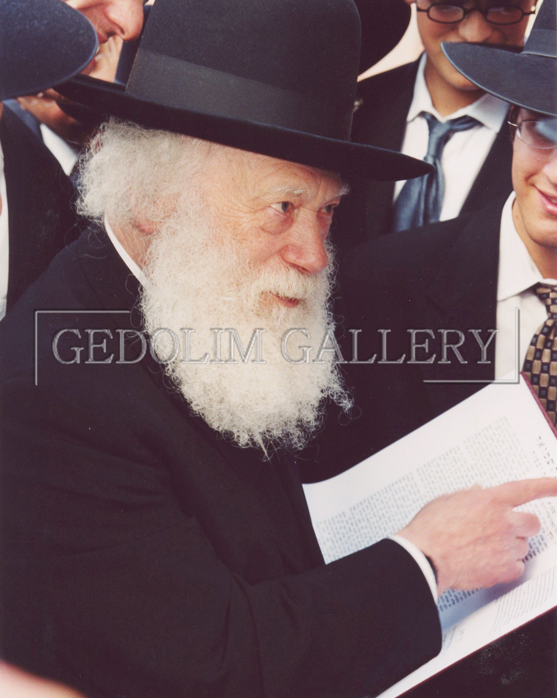 A man with a beard is holding a piece of paper in front of a gedolim gallery logo