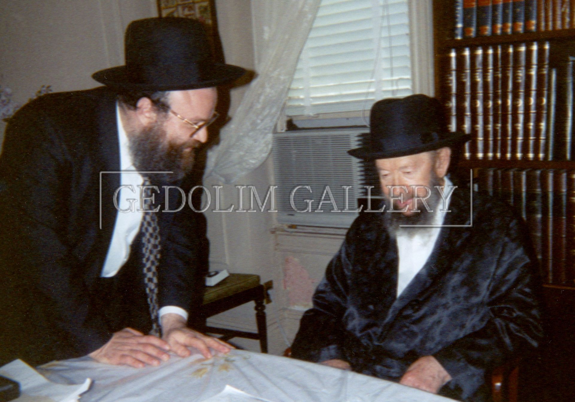 Two men are standing next to each other in front of a bookshelf that says gedolin gallery