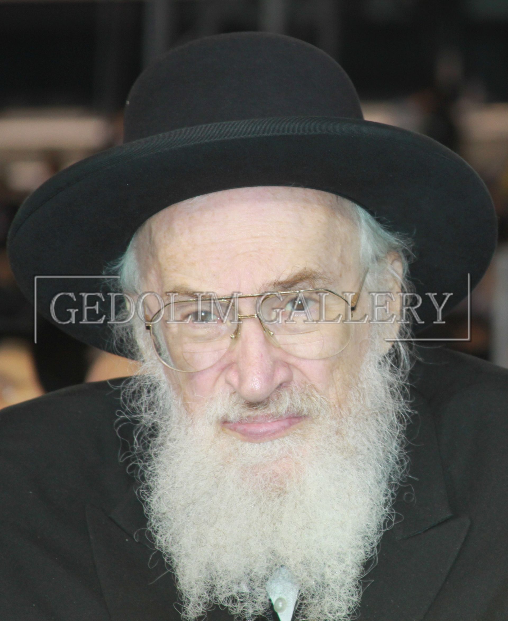 A man with a beard and glasses is wearing a black hat